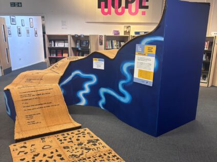 Final 'You're Welcome' sculpture. A series of undulating waves, made from a wooden frame with blue painted sides, onto of which sit welcome mats printed with poems create by participating primary school pupils.
