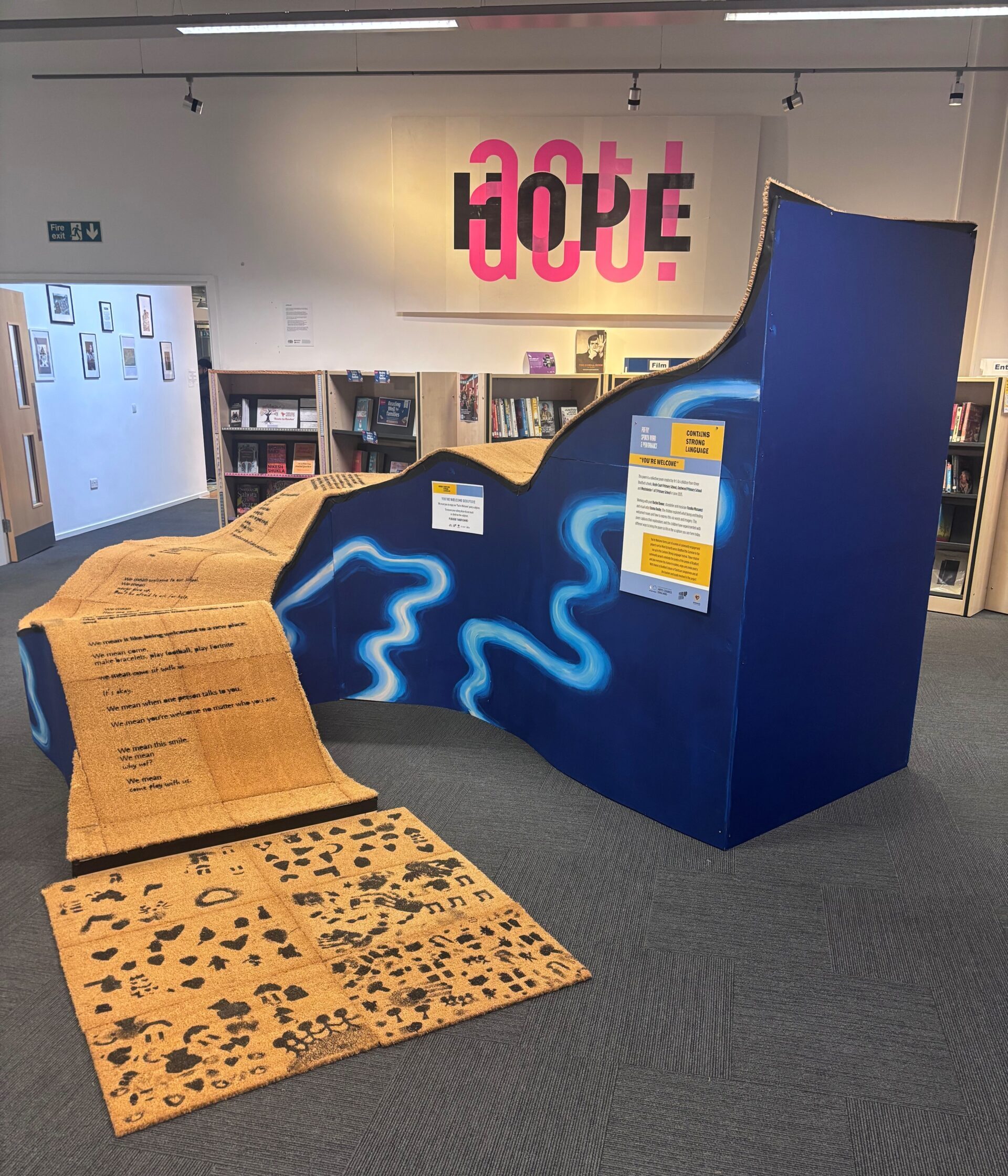 Final 'You're Welcome' sculpture. A series of undulating waves, made from a wooden frame with blue painted sides, onto of which sit welcome mats printed with poems create by participating primary school pupils.