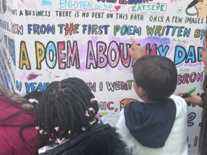 Two children adding drawings to the Bards of Bradford interactive Doodle Wall in Broadway Shopping Centre, Sep 2025.