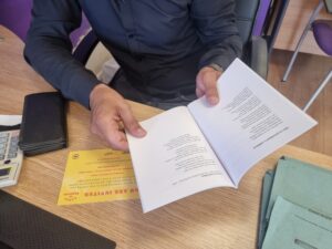 The hands of a man hold a booklet containing verses of poetry.