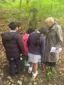 A group of children listen to stories about the wood told by a Friends of Park Wood volunteer